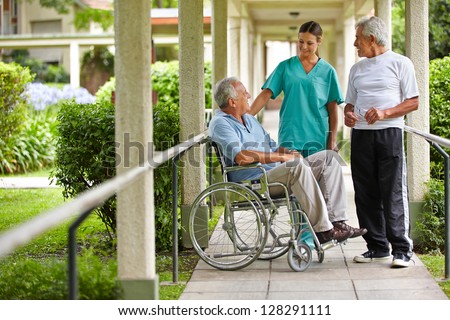 Two Senior Citizens Talking To A Nurse In A Hospital Garden
