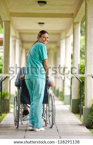 Smiling nurse pushing senior man in wheelchair in a nursing home