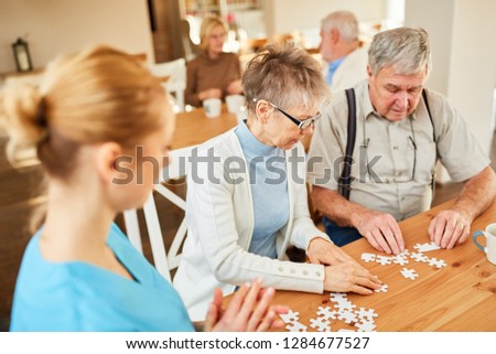 Senior couple playing puzzle in the nursing home cared for by a geriatric nurse