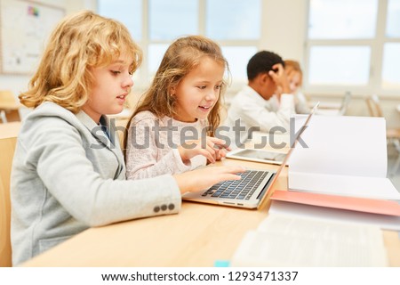 Children work together on laptop computer online in elementary school