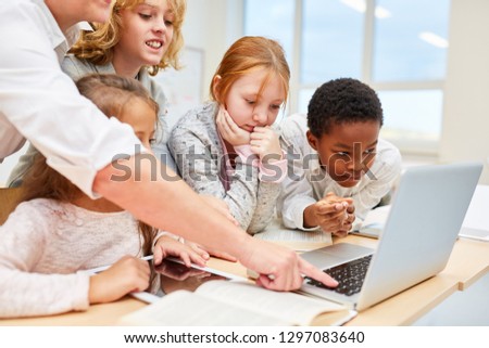 Teacher helps student team at work on laptop in computer lesson