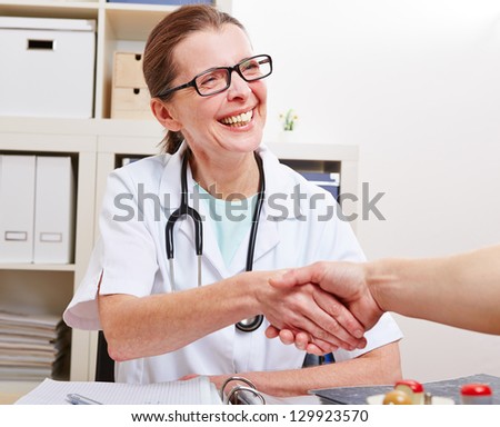 Happy senior female doctor giving handshake to a patient in her office