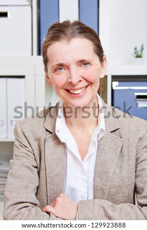 Elderly happy business woman sitting in her office at her desk