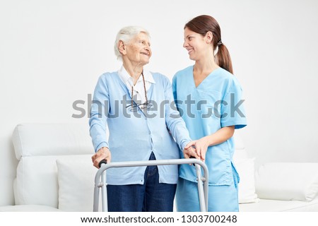 Old woman learns to walk with a walker and is supported by caregiver