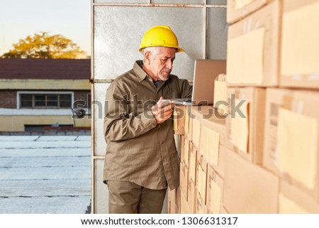 Senior as warehouse specialist with computer in warehouse with packages for shipping
