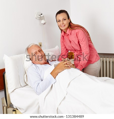 Smiling woman visiting old bedridden man in a hospital bed