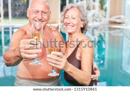 Happy senior couple on spa vacation celebrating with sparkling wine in the swimming pool