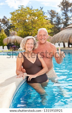Smiling senior couple is standing with thumbs up in the pool of wellness hotel
