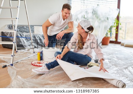 Young couple is having fun at wallpapering and painting in new home
