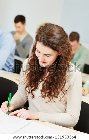 Happy female student taking notes in university course classroom