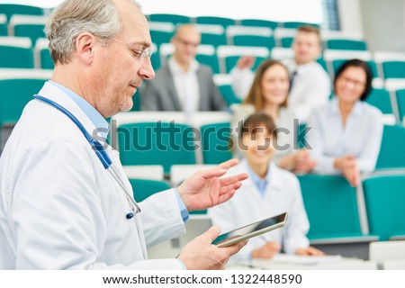 Senior medicine lecturer with tablet training doctors in university lecture hall