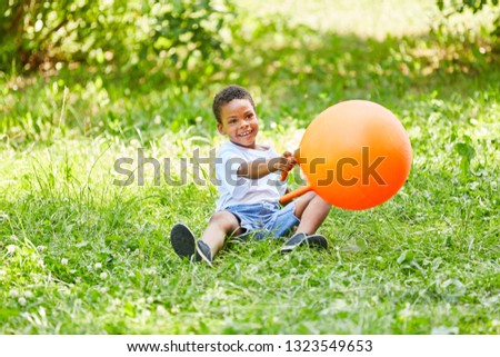 African boy is playing with a bouncy ball on a meadow in summer