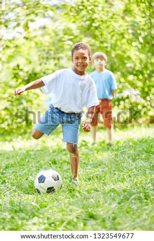 African boy is playing football with a friend in the park in summer
