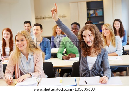 Happy student raising her hand and answering question in university class