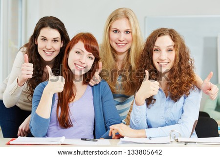 Four attractive happy women holding their thumbs up in university