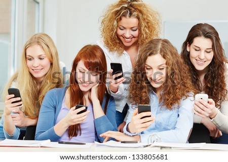Many happy girls using social media with their smartphones in school