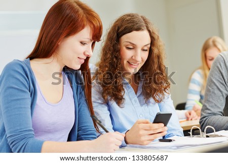 Two young women looking at their smartphone in university class