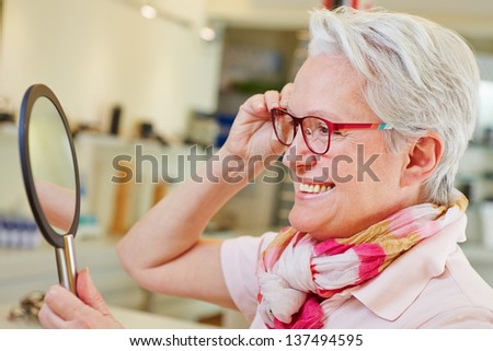 Happy elderly woman with new glasses looking in a mirror at optician store