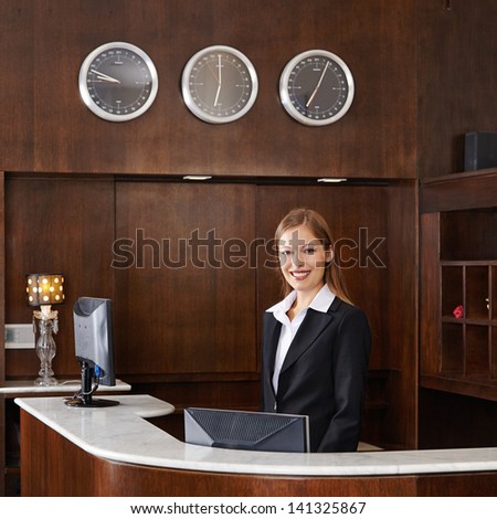 Happy Female Receptionist Behind Counter At Hotel
