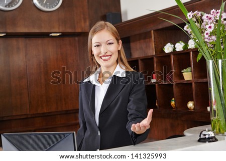 Smiling receptionist behind desk in hotel offers welcome to guest