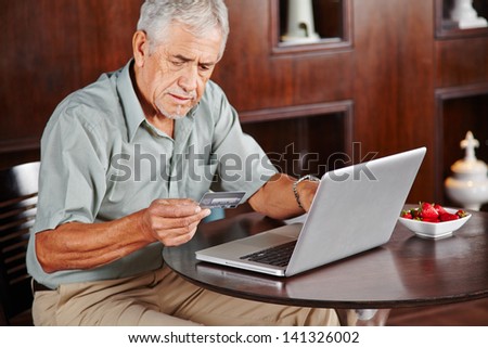 Senior man at laptop paying with credit card for online shopping