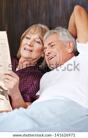 Two senior people reading newspaper together in a bed