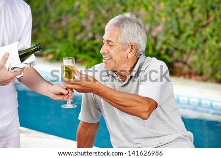 Senior man getting glass of champagne from waiter at pool