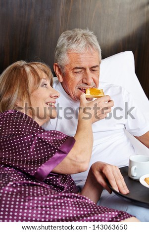 Happy elderly couple having breakfast together in a hotel bed