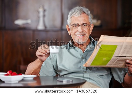 Happy senior man sitting with coffee and newspaper in a cafÃ?Â?Ã?Â©