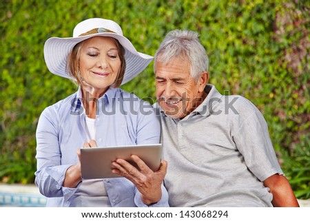 Two happy senior people sitting with tablet computer at pool