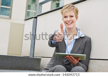 Young happy business woman with tablet computer holding thumbs up