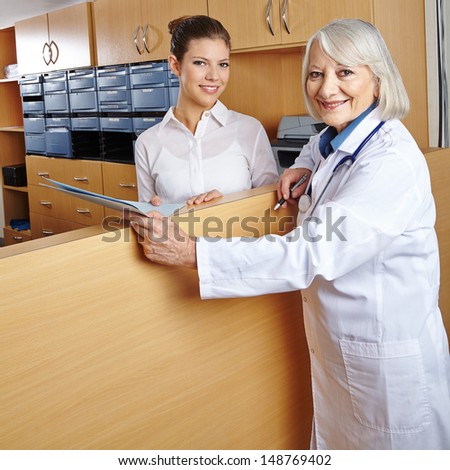 Elderly female doctor with receptionist at hospital reception