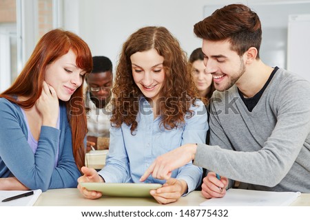 Three happy students learning in class with a tablet PC in classroom