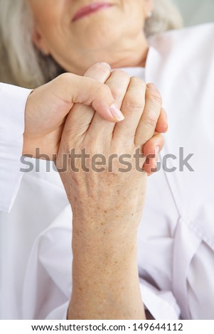 Doctor holding hand of senior woman patient for comfort in a hospital