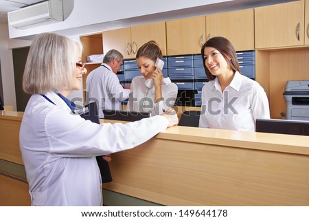 Senior Doctor Talking With Receptionist At Hospital Reception
