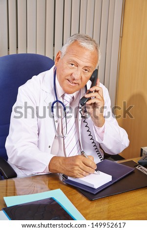 Senior doctor taking notes during phone call in his hospital office