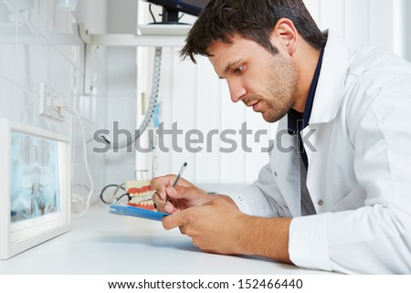Dentist with x-ray image of teeth taking some notes in his dental practice