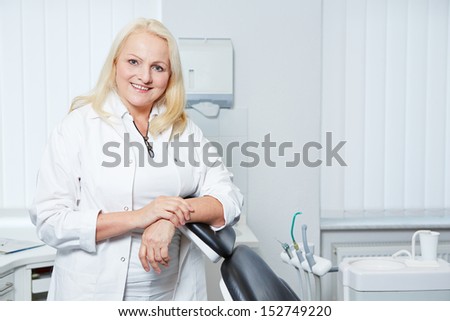Smiling senior denist standing in her dental practice at chair