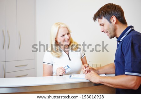 Patient talking with doctors assistant at the reception while filling out a form