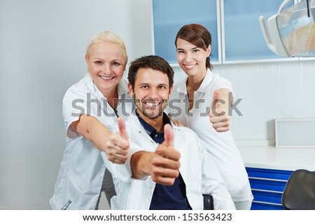 Happy dentist and smiling dental team holding their thumbs up in dental practice