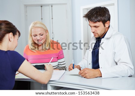 Doctor and elderly patient standing at reception with doctors assistant