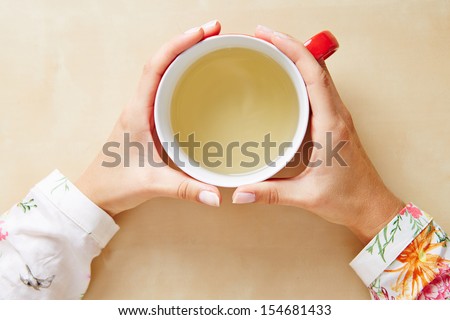 Two hands holding chamomile tea in a cup from above