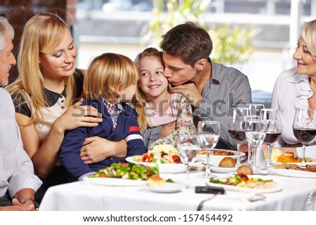 Father kissing daughter in restaurant while eating out with the family
