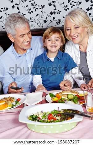 Happy little child eating with his grandparents at the dinner table