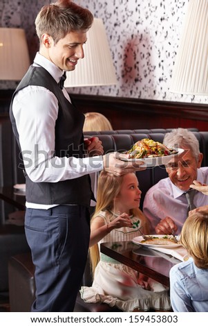 Waiter serving food to family in a restaurant