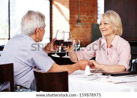 Elderly couple clink glasses with red wine in a restaurant