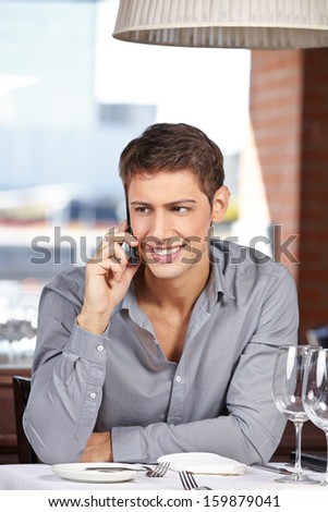 Happy businessman making call with his smartphone in a restaurant
