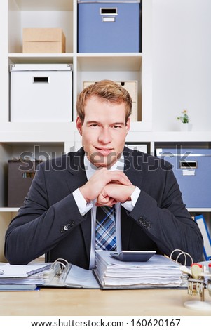 Smiling business man sitting at desk in office with files