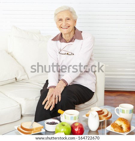 Old smiling woman sitting at set breakfast table at home
