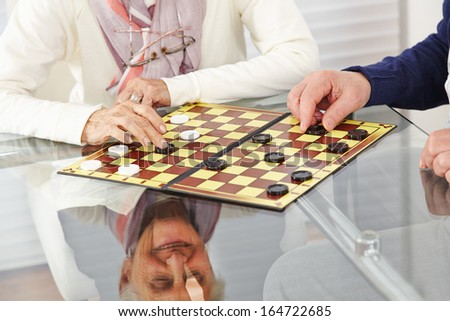 Happy senior citizen couple playing checkers at home
